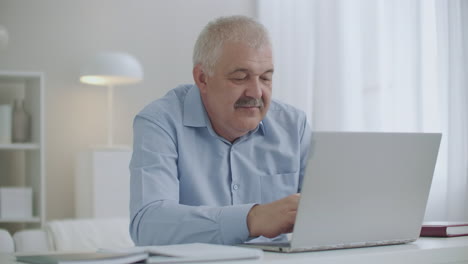Ein-Mann-Mittleren-Alters-Mit-Schnurrbart-Tippt-Text-Auf-Der-Tastatur-Eines-Laptops,-Surft-Im-Internet-Und-Arbeitet-Mit-Einem-Notebook-Von-Zu-Hause-Aus
